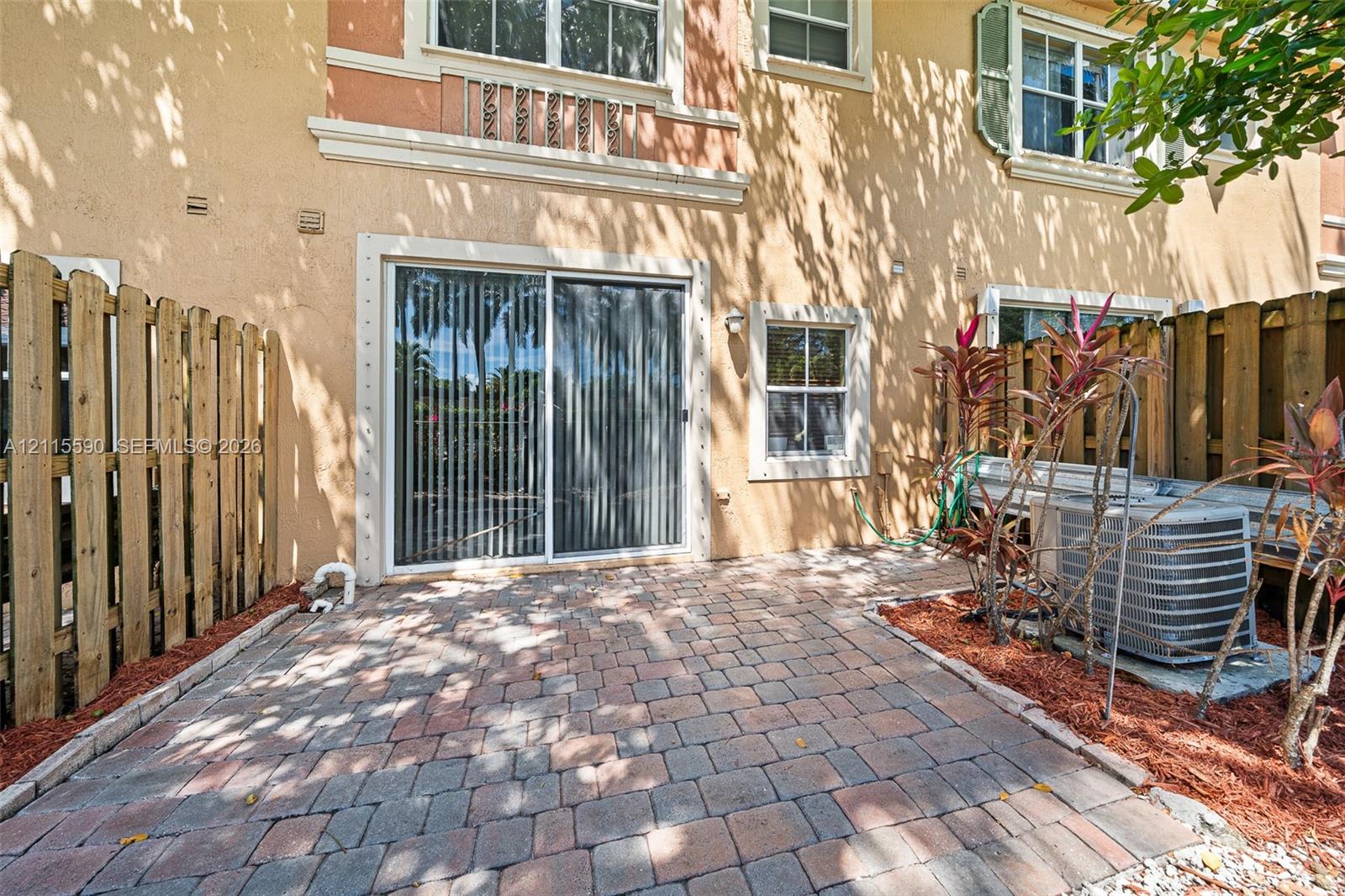 Private rear patio featuring stone paver flooring, enclosed by vertical wood privacy fencing and sliding glass doors