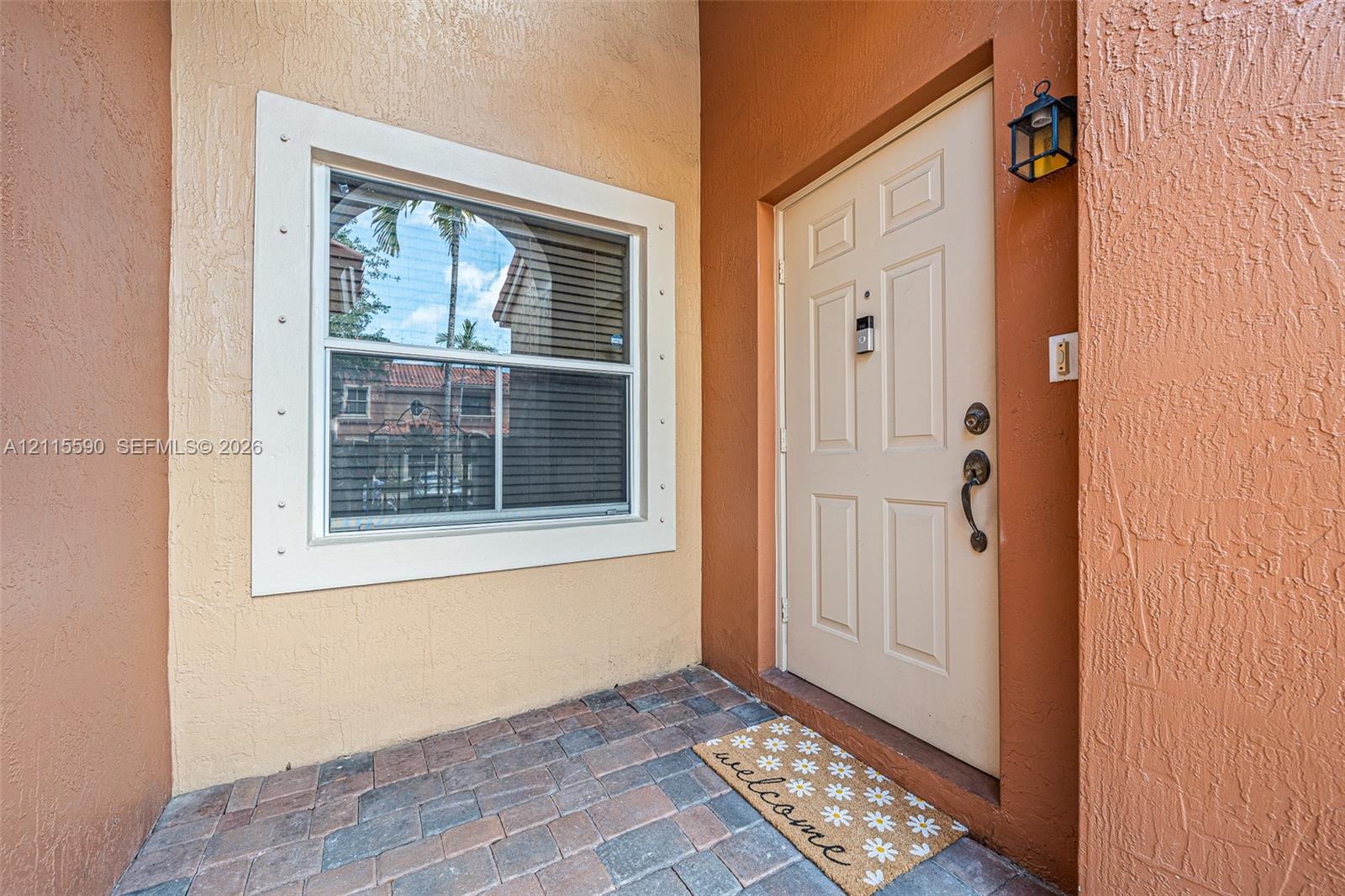 Entryway featuring a paver-stone landing, a six-panel exterior door with integrated hardware, and a window with a wide, custom-trimmed surround