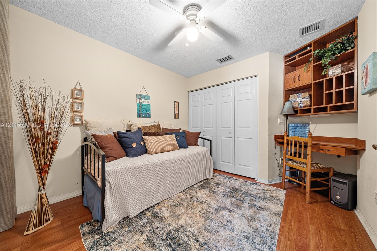 Wood-finish flooring, ceiling fan with integrated light fixture, built-in wooden desk with overhead shelving, and double-door closet