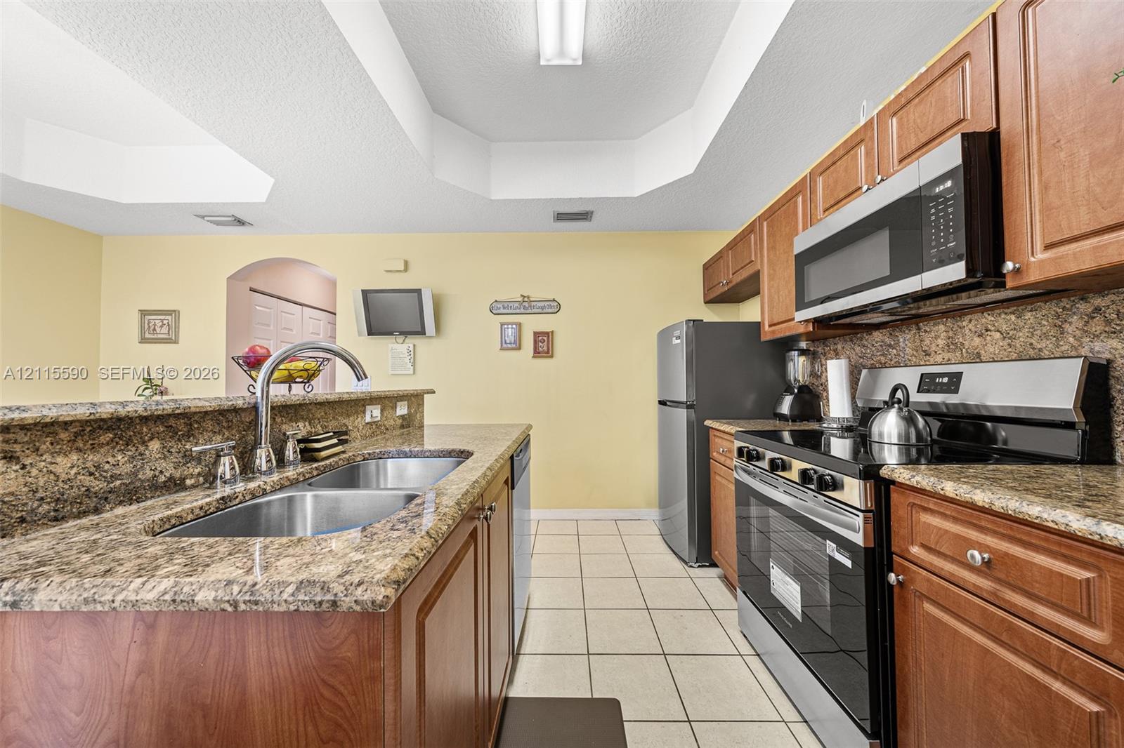 Kitchen featuring stained wood cabinetry, stone-finish countertops, stainless steel appliances, dual-basin stainless steel sink, and ceramic tile flooring