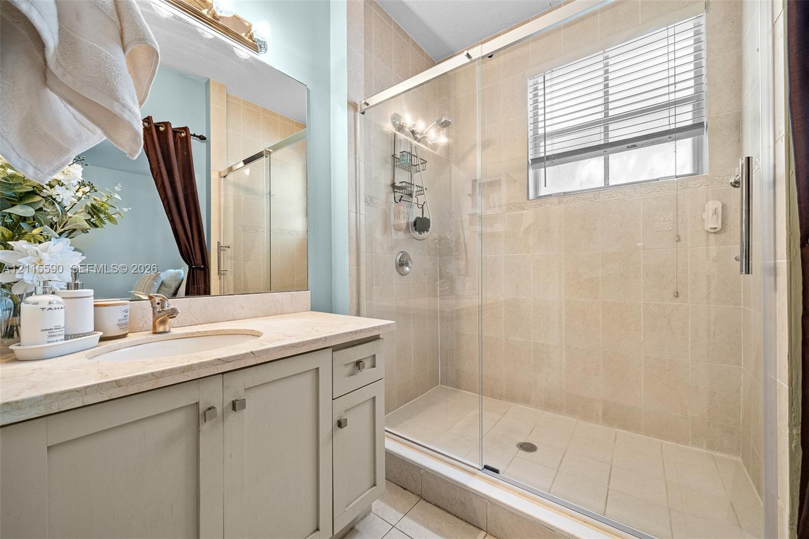 Bathroom featuring a vanity with an integrated sink and neutral countertop, walk-in shower with floor-to-ceiling tile, sliding glass shower door, and wall-mounted vanity mirror with integrated lighting