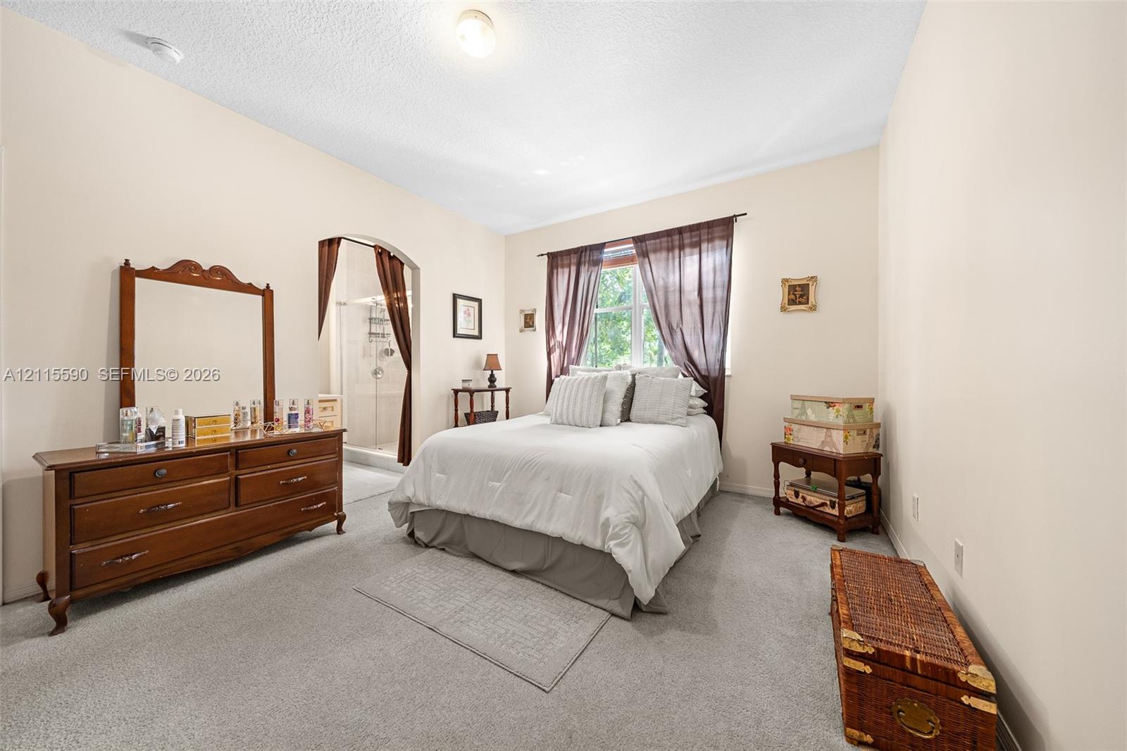 Room featuring neutral wall tones, wall-to-wall carpeting, an arched doorway, and a window with wood-frame trim