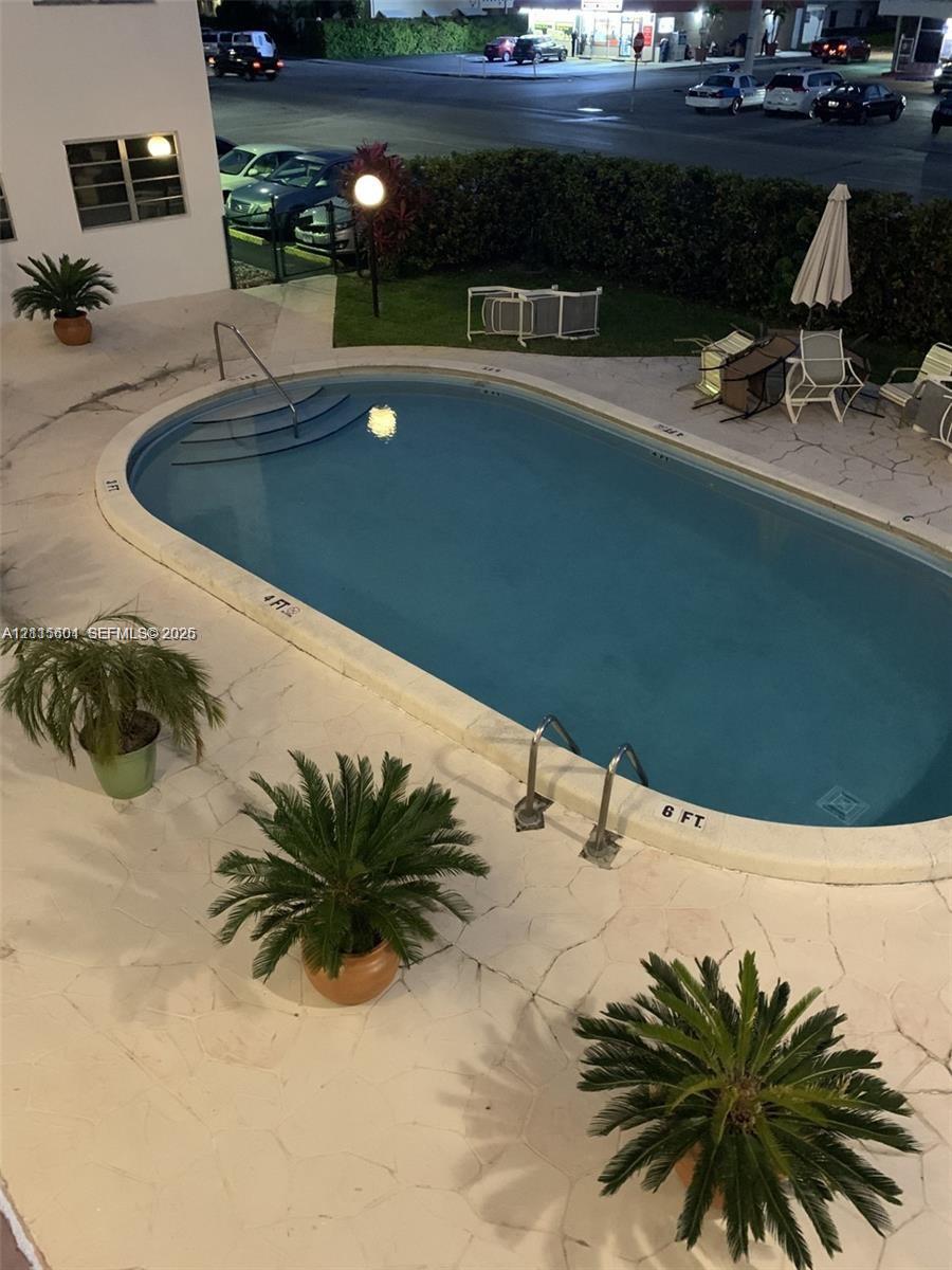 Oval swimming pool featuring a concrete deck, metal handrails, and integrated steps, surrounded by mature landscaping