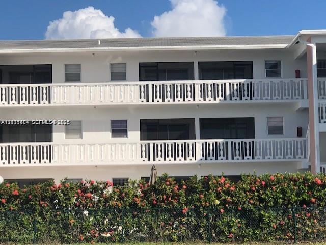 Multi-story exterior featuring white stucco facade, screened balconies with decorative railings, and mature landscaping
