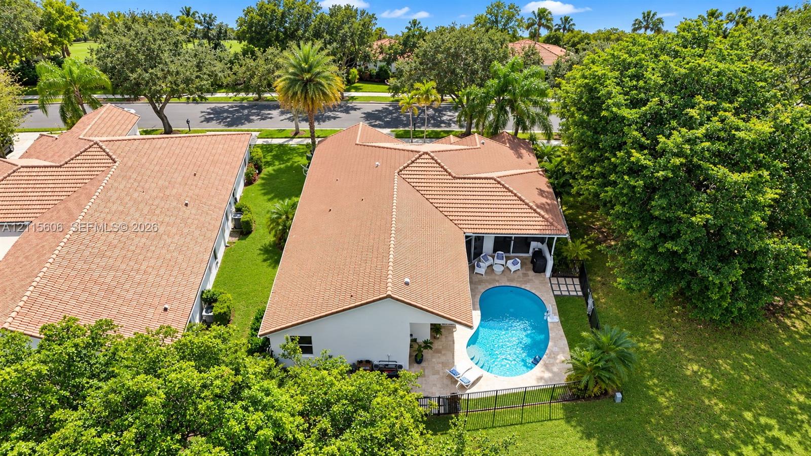Aerial perspective of a property featuring a tile roof, an in-ground pool with a paved patio, and a landscaped lot with mature trees