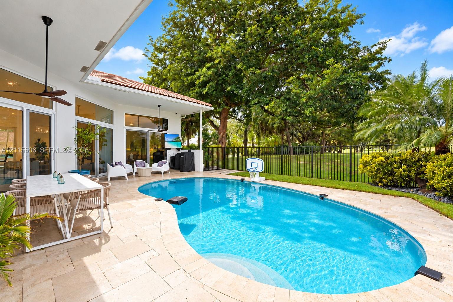 Covered outdoor patio featuring stone pavers, a kidney-shaped in-ground swimming pool, metal perimeter fencing, and floor-to-ceiling glass panel doors