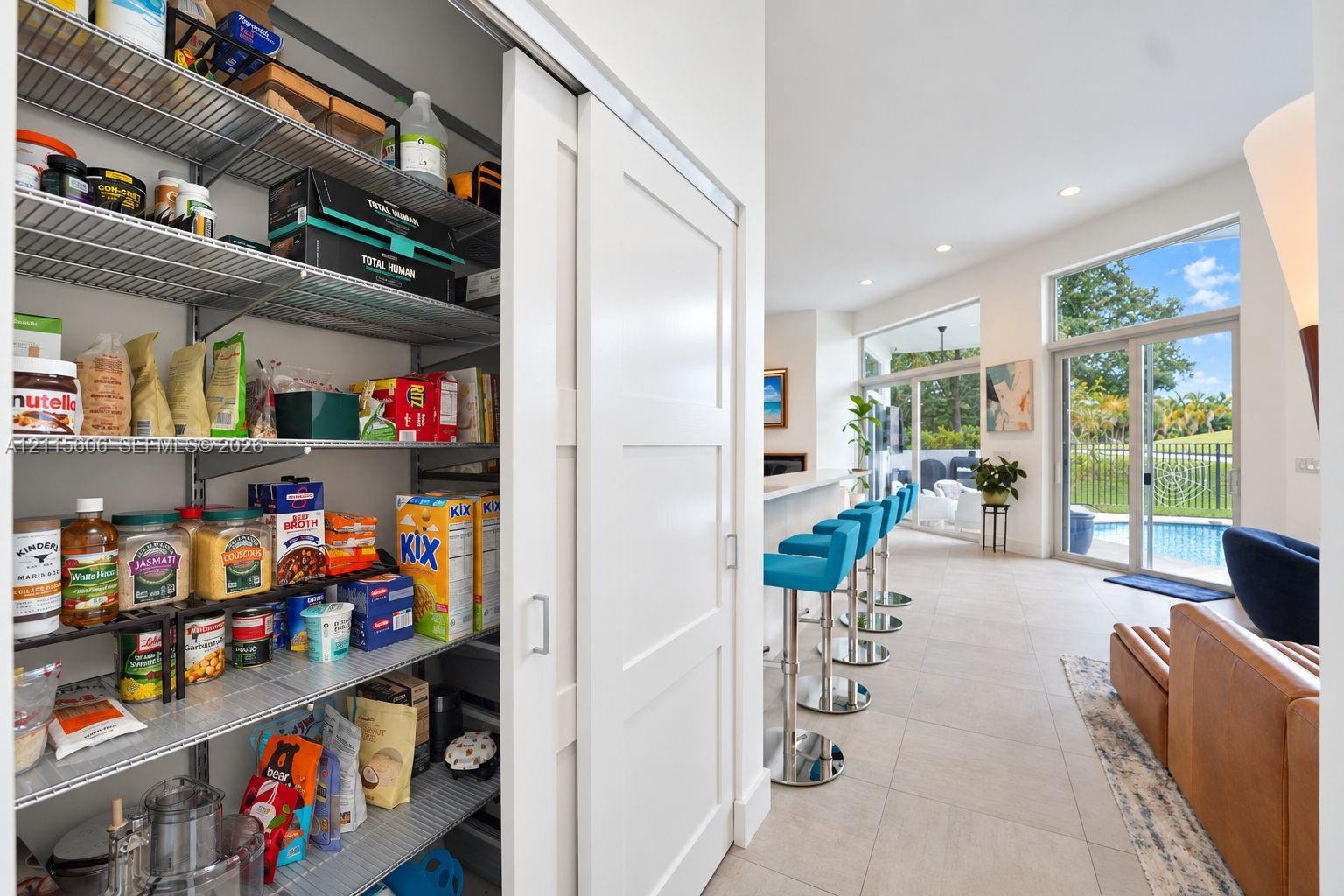 Walk-in pantry featuring adjustable wire shelving and a sliding shaker-style door, highlighted by neutral tile flooring, recessed lighting, and expansive floor-to-ceiling glass sliding doors
