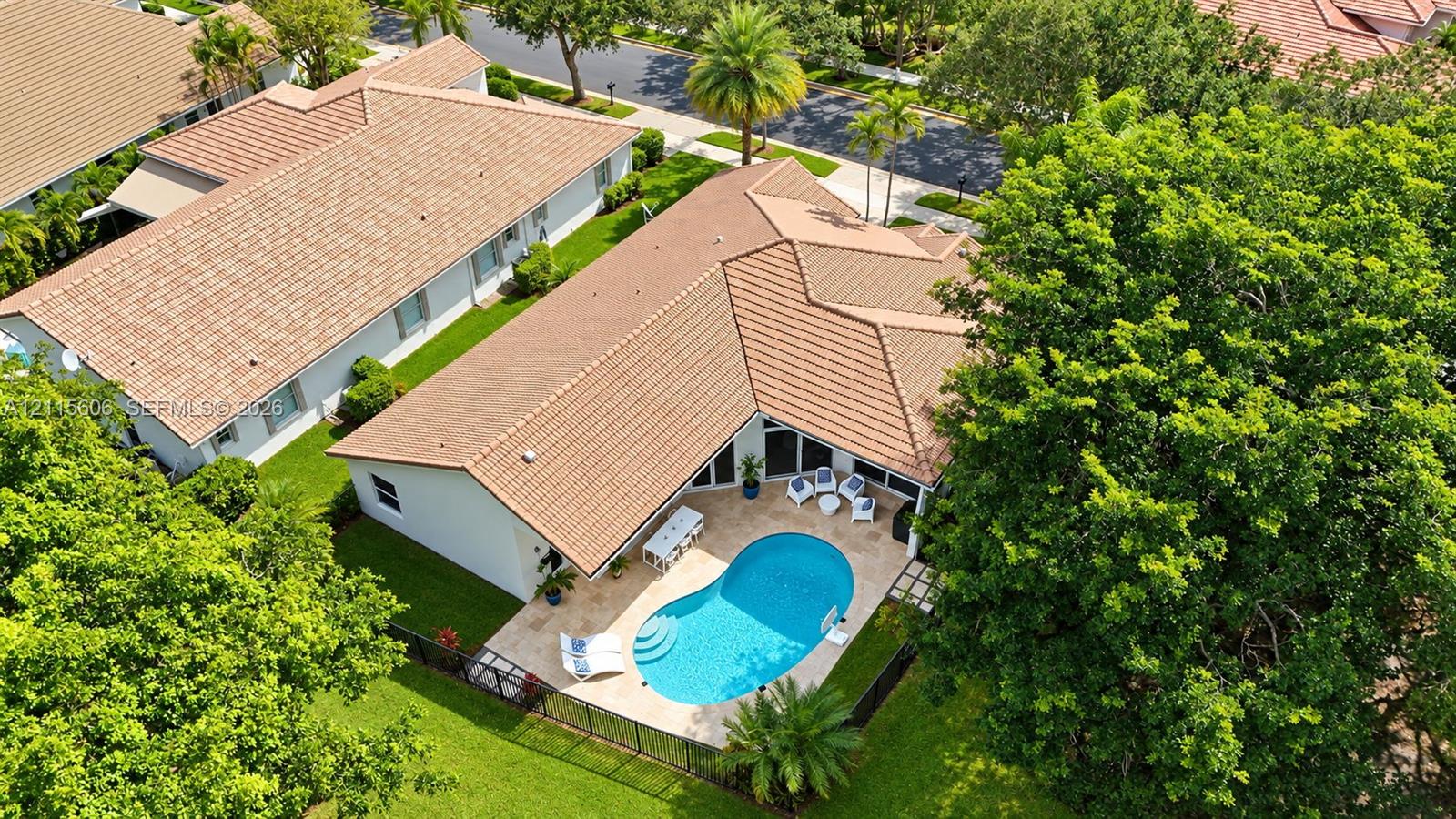 Aerial perspective of a residence featuring a clay tile roof, a private swimming pool with built-in entry steps, a stone-paved patio, and a fenced yard with mature trees
