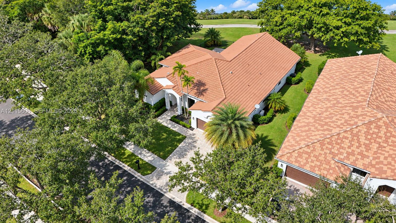 Tile roof architecture, paver driveway, manicured landscaping, and mature trees on a corner lot