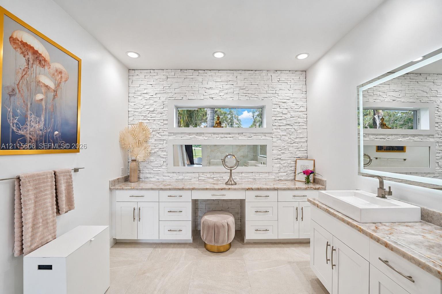 Stone-veneer feature wall with stacked horizontal windows, white cabinetry with integrated vanity, rectangular vessel sink, and illuminated vanity mirror