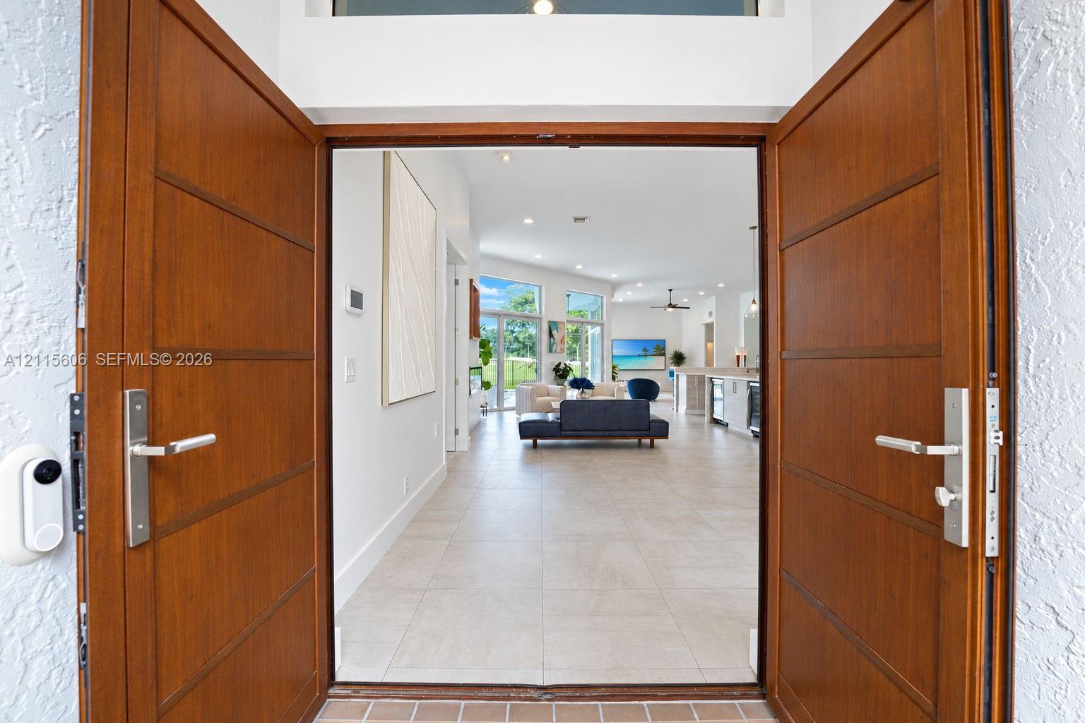 Double wood-finish entry doors featuring horizontal paneling and brushed metal hardware, complemented by a transom window and large-format tile flooring