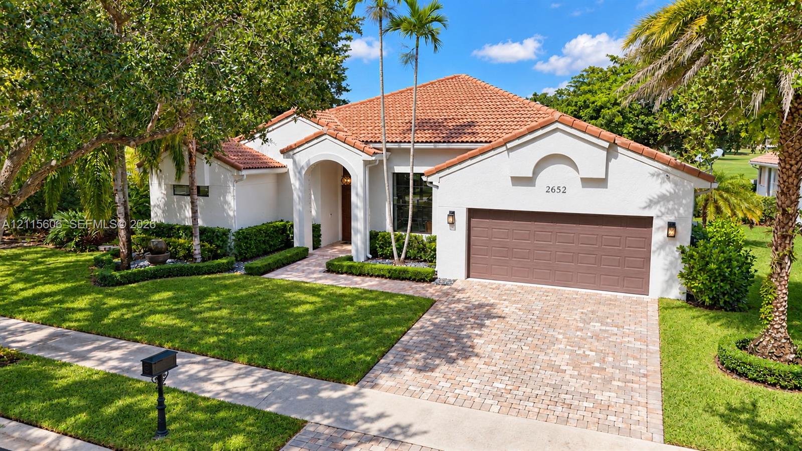 Stucco exterior featuring a red tile roof, arched entryway, paved driveway, and curated landscaping