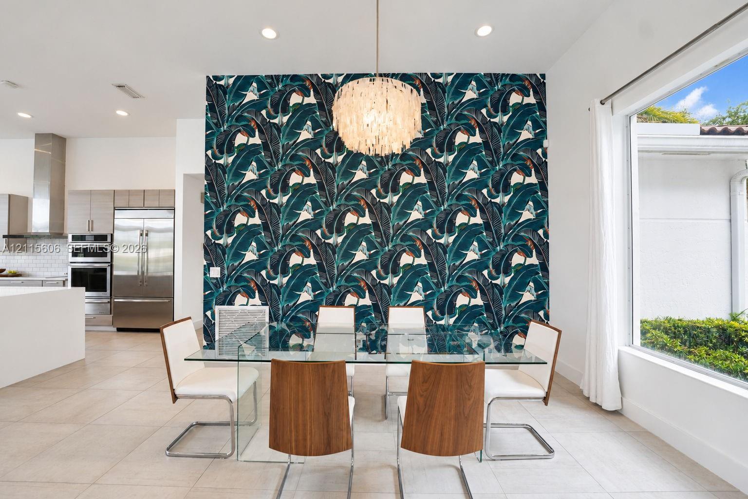 Dining area featuring a statement wall with botanical patterned wallpaper, a tiered shell pendant light, recessed ceiling lighting, large-format tile flooring, and a floor-to-ceiling window