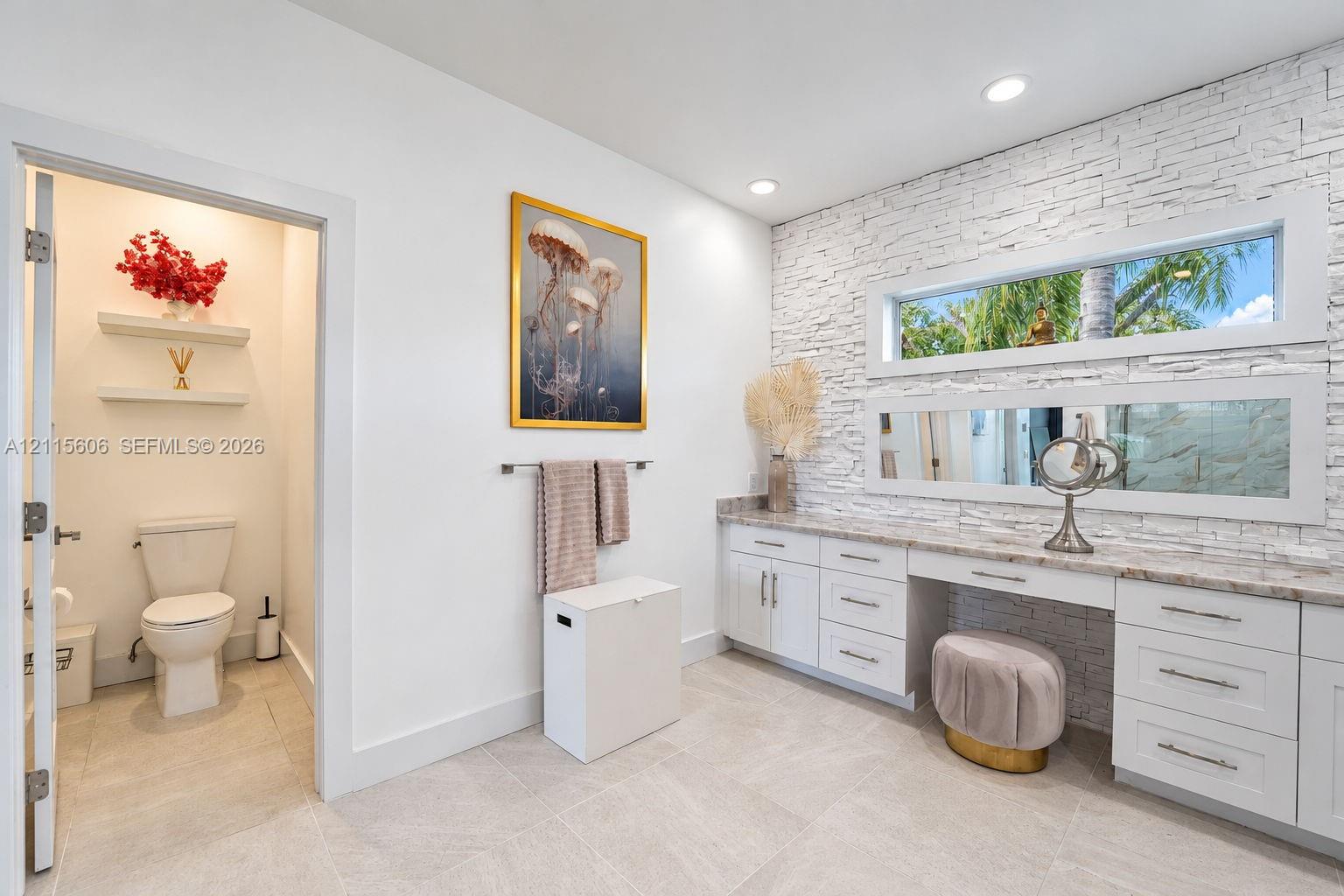 Textured stone accent wall featuring horizontal ribbon windows, white shaker-style cabinetry with neutral stone countertops, and tile flooring