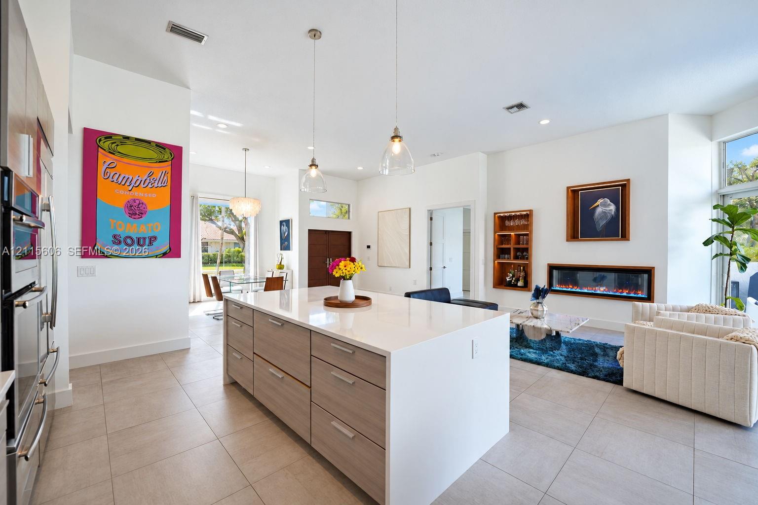Large kitchen island with a neutral-toned countertop and wood-finish cabinetry, linear built-in fireplace, recessed lighting, and tile flooring