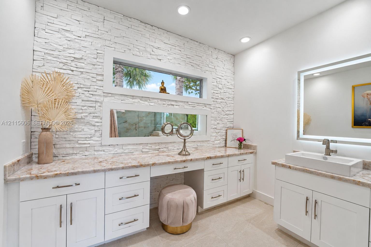 Stacked stone accent wall featuring dual horizontal windows, custom white cabinetry, stone-finish countertops, and a rectangular vessel sink with a wall-mounted faucet