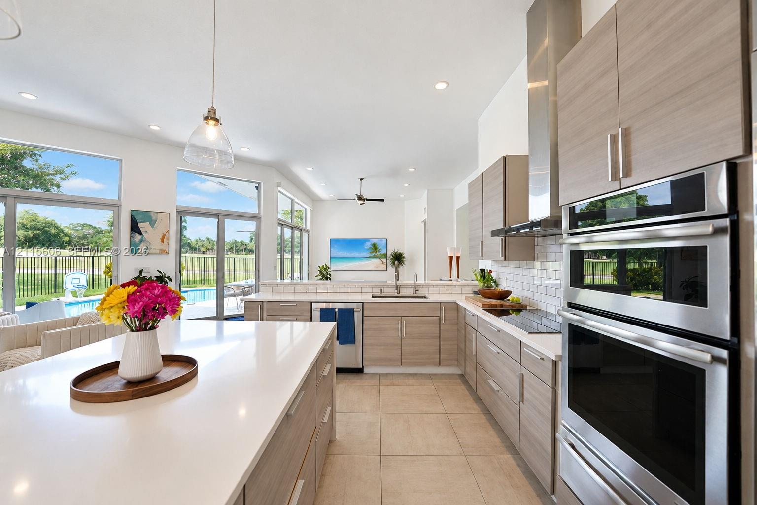 Kitchen featuring a large central island with a quartz countertop, wood-finish cabinetry, stainless steel double wall ovens, a white subway tile backsplash, and floor-to-ceiling windows