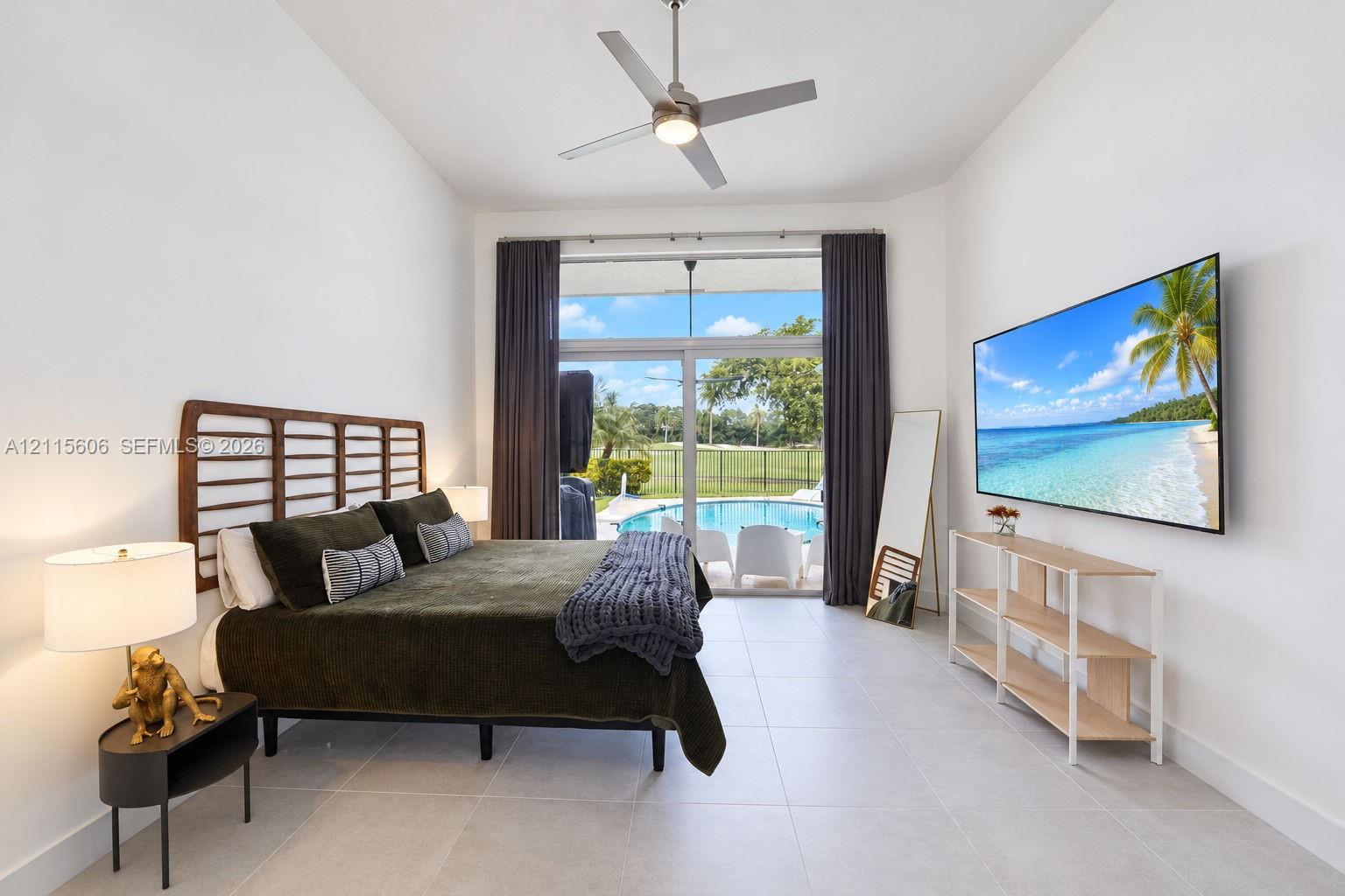 High-ceilinged room featuring large-format tile flooring, a brushed metal ceiling fan, and floor-to-ceiling sliding glass doors opening to an exterior swimming pool and patio area
