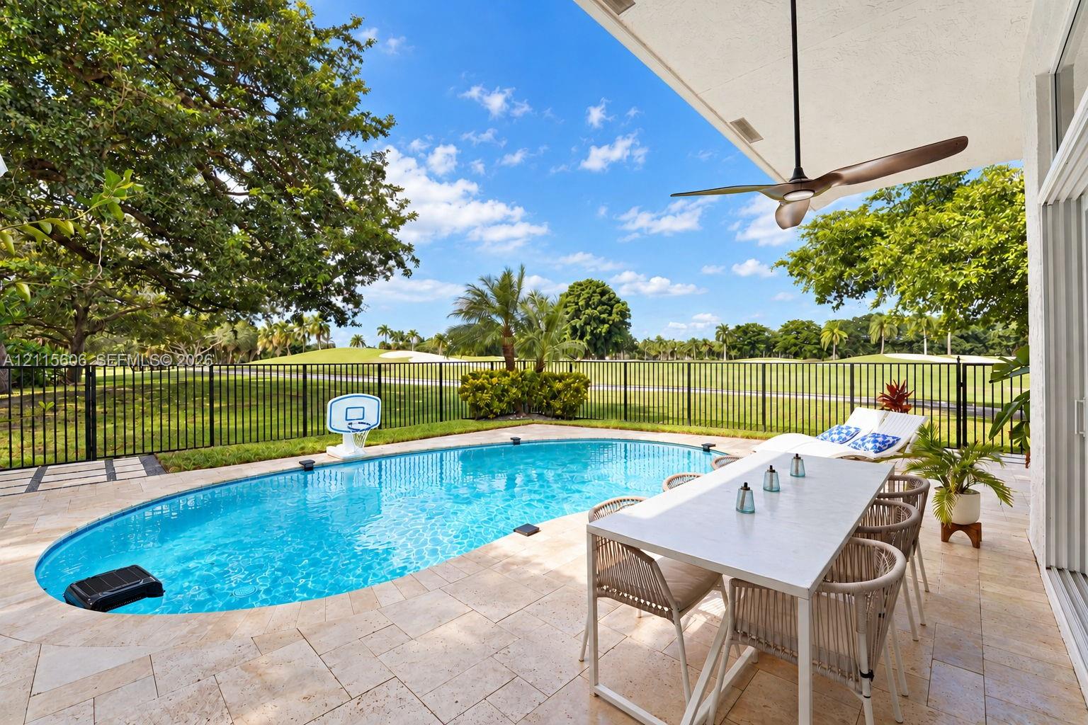 Covered patio featuring a ceiling fan, stone-tile flooring, an in-ground pool, and metal perimeter fencing