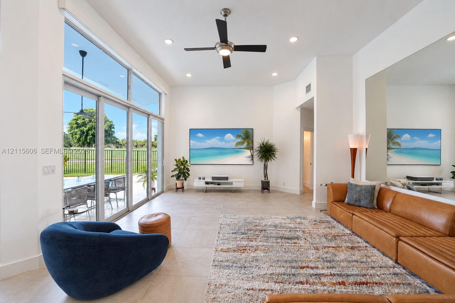 High-ceiling living space featuring floor-to-ceiling glass sliding doors, large-format tile flooring, a mounted ceiling fan with integrated lighting, and a full-length wall mirror