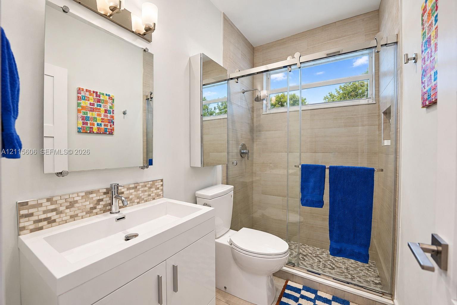 Modern vanity with rectangular sink and mosaic tile backsplash, frameless glass shower enclosure, horizontal tile shower surround, and integrated wall mirror