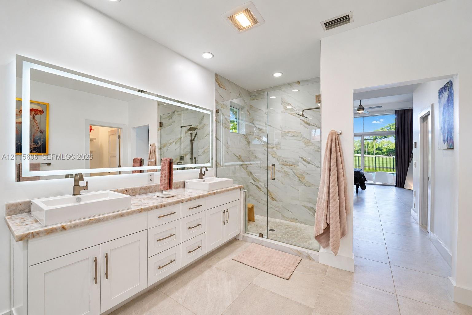 Dual-sink vanity with rectangular vessel basins, stone countertop, large LED-backlit mirror, and glass-enclosed shower with tiled wall surfacing