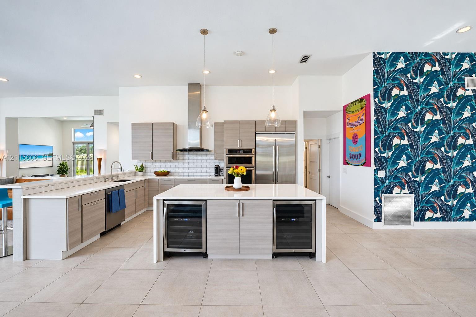 Kitchen featuring light-finish slab cabinetry, quartz countertops, stainless steel appliances, a central island with dual under-counter wine refrigerators, and pendant lighting