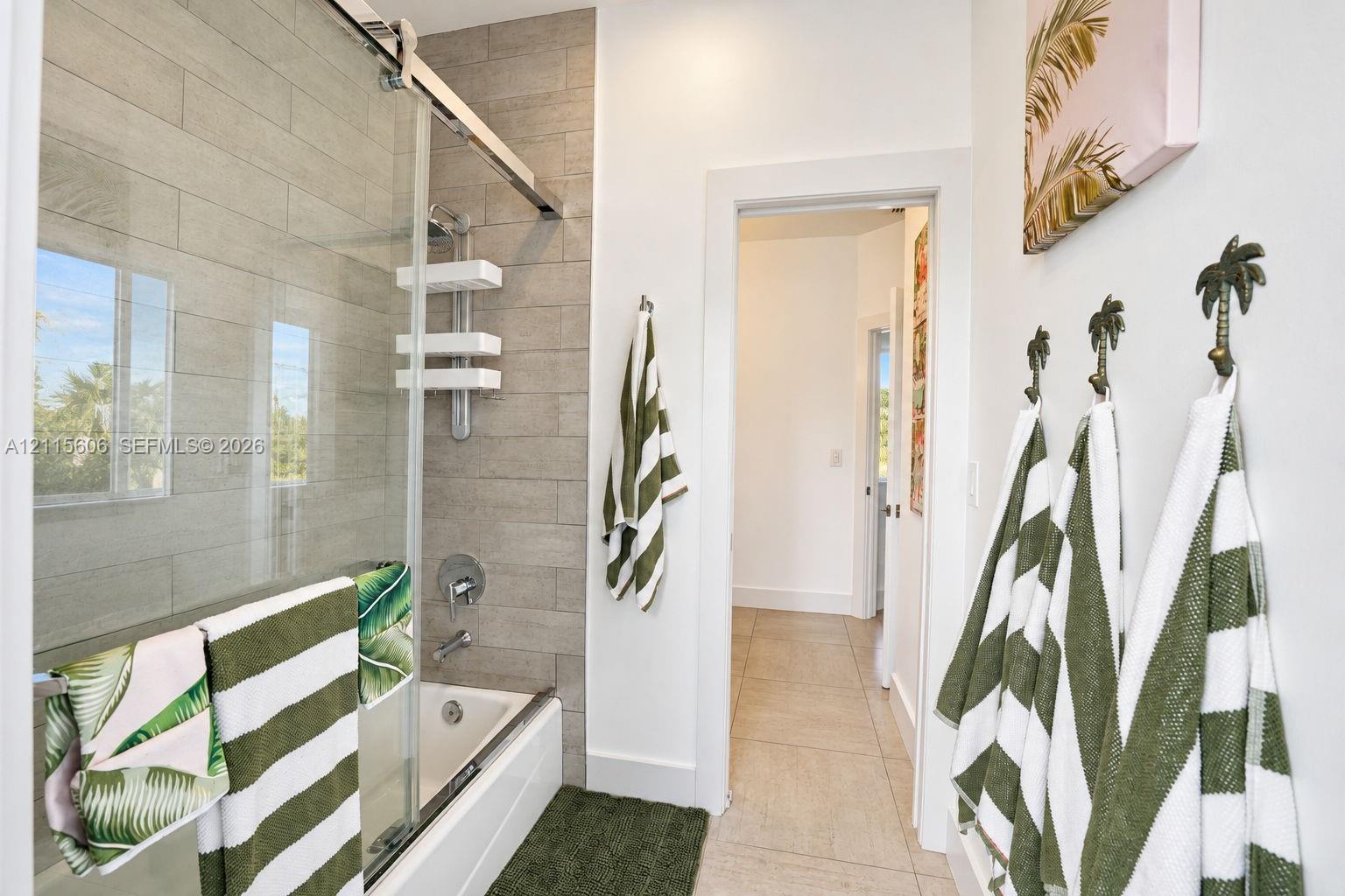 Bathroom featuring a shower-tub combination with a glass sliding door enclosure, tiled wall surround, and large-format floor tile