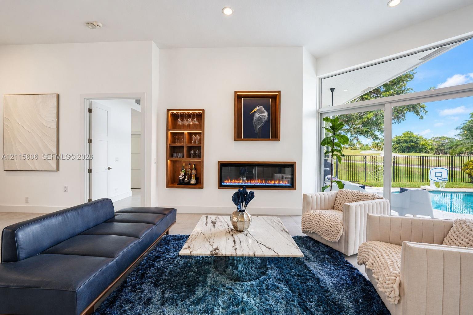 Modern living space featuring a built-in electric fireplace, recessed wood-trimmed shelving, large-format tile flooring, and floor-to-ceiling glass sliding doors with pool and golf course exposure