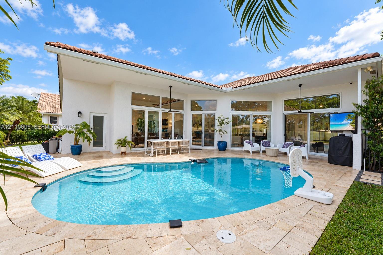 Outdoor living area featuring a custom-shaped swimming pool with built-in steps, expansive stone paver patio, covered loggia, and large-scale glass sliding doors