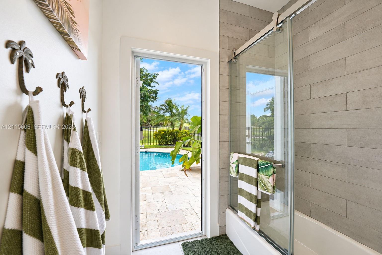 Bathroom featuring a sliding glass shower door, rectangular tile wall surround, and exterior door with access to a patio and pool