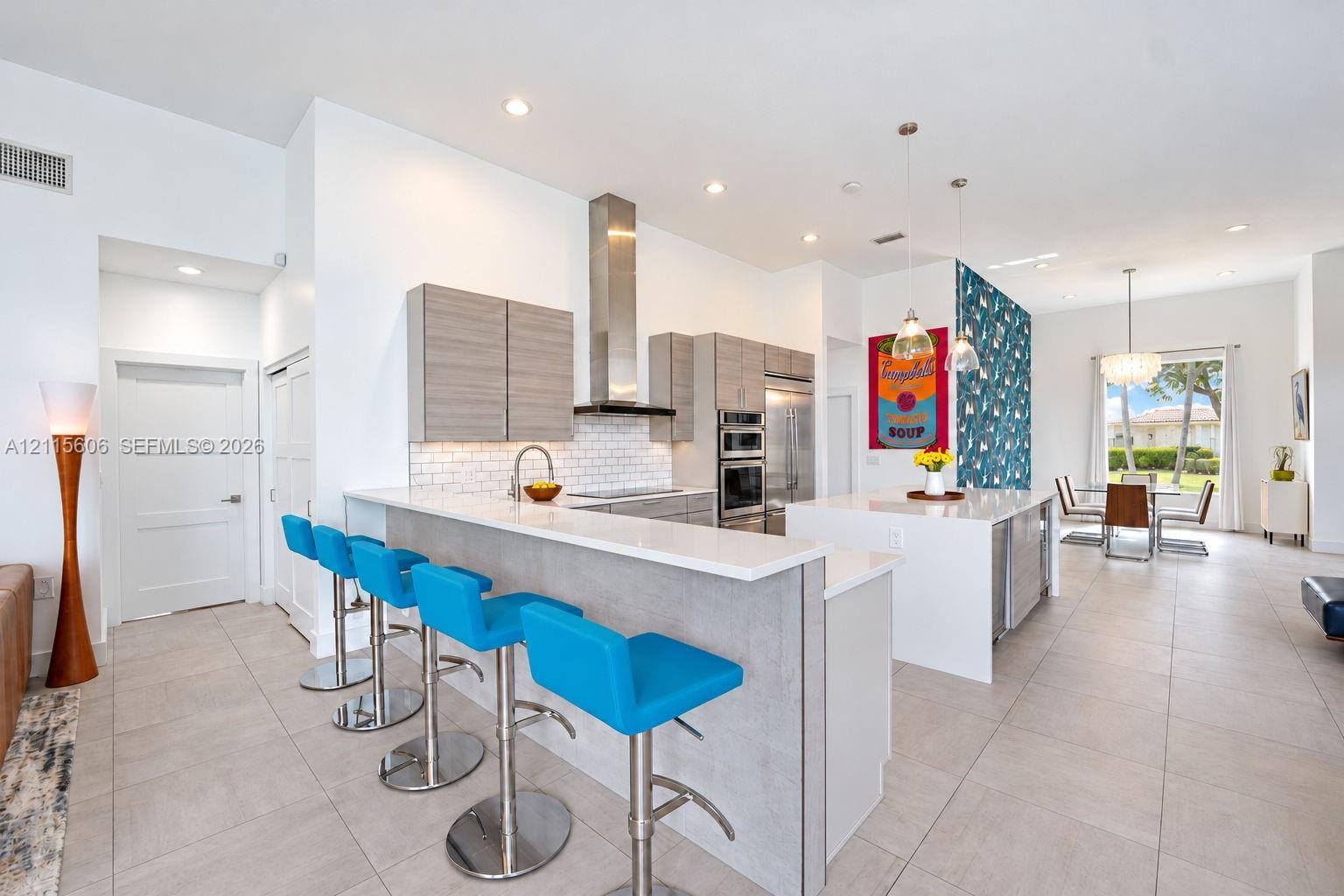 Kitchen featuring flat-panel cabinetry, a quartz-topped island with waterfall edge, stainless steel appliances, a white subway tile backsplash, and oversized floor tiles
