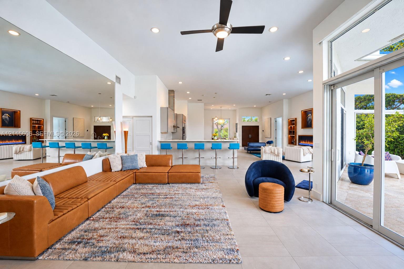 Open-concept interior featuring large-format tile flooring, expansive glass sliding doors, dual built-in fireplaces, a ceiling fan, and recessed lighting throughout