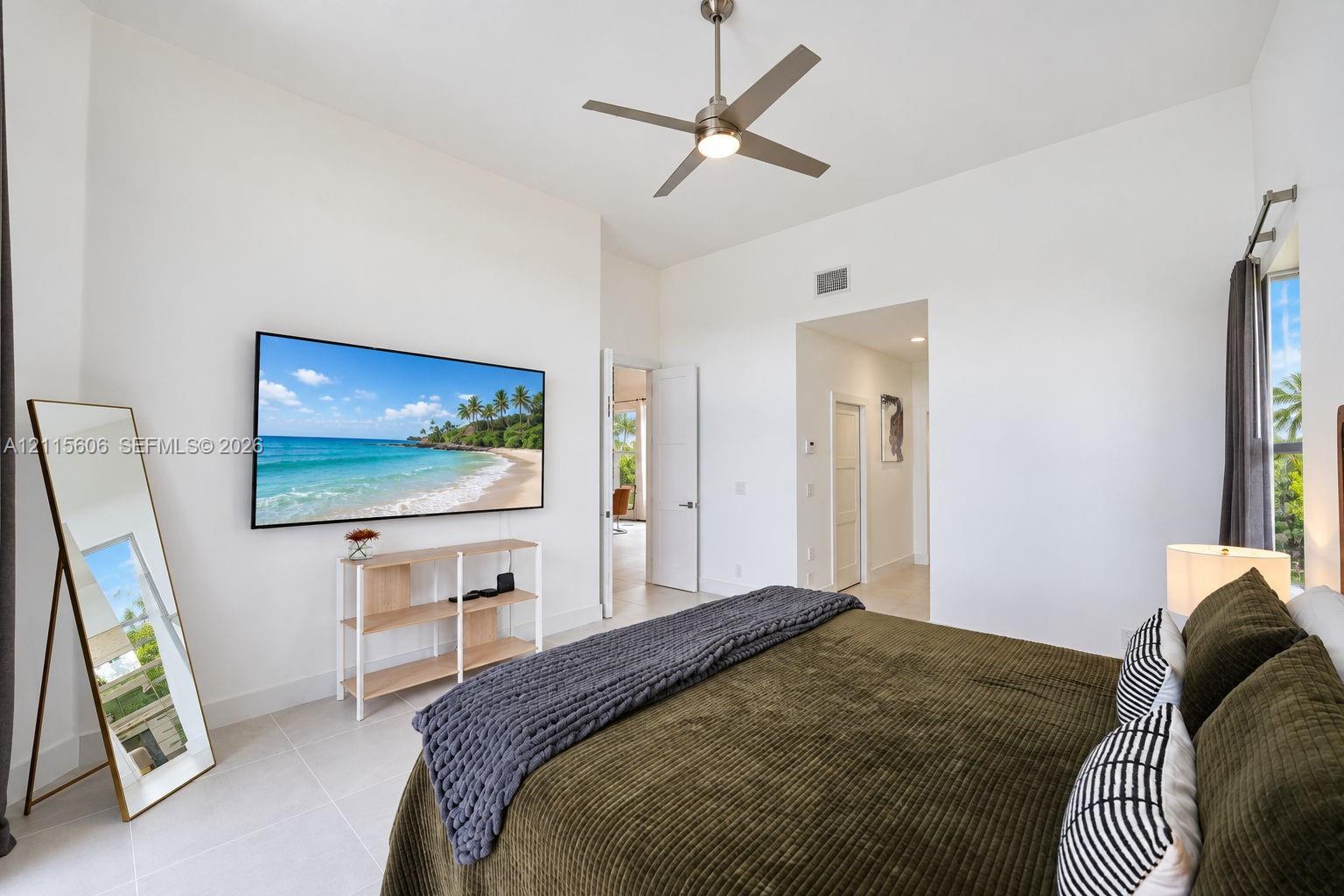 High-ceilinged room featuring neutral tile flooring, a brushed-nickel ceiling fan, and large windows with prominent natural light
