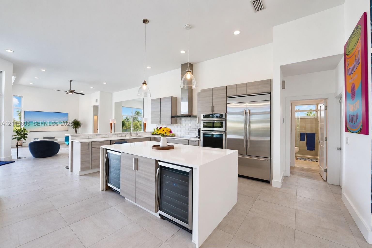 Kitchen featuring light-finish cabinetry, a large central island with a solid surface countertop, stainless steel appliances, dual beverage coolers, and pendant lighting