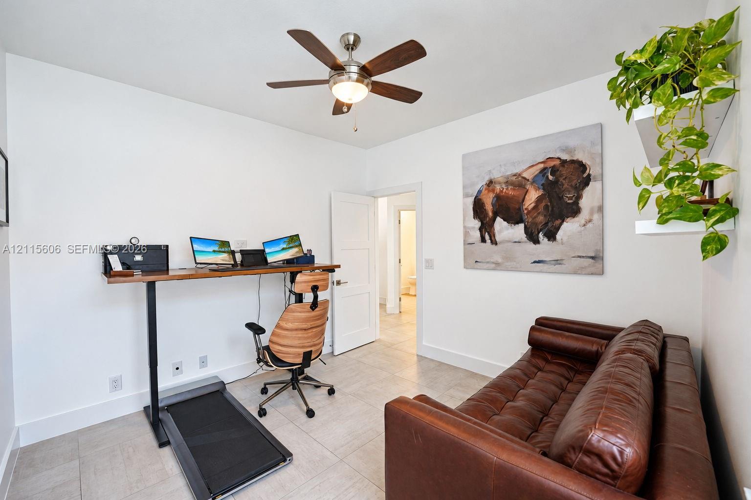 Neutral-toned tile flooring, white shaker-style interior door, and multi-blade ceiling fan with integrated light fixture