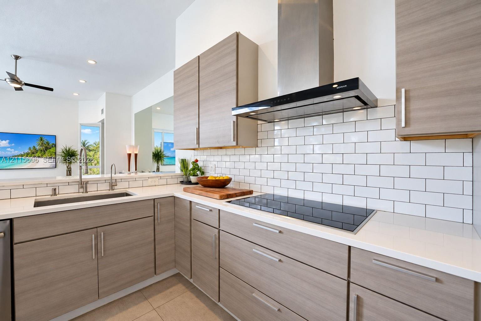 Kitchen featuring flat-panel wood-finish cabinetry, quartz countertops, white subway tile backsplash, stainless steel range hood, and integrated induction cooktop