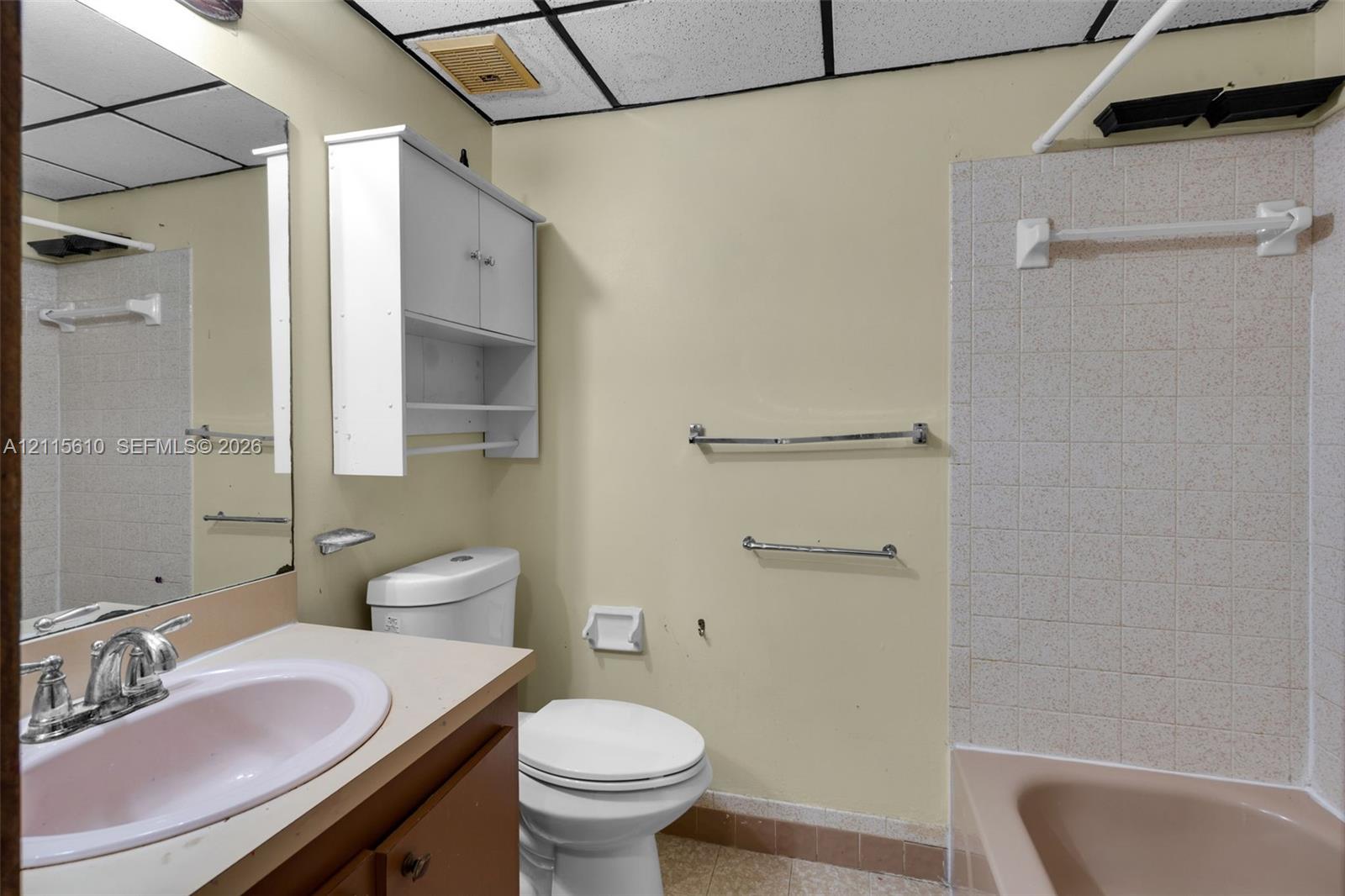 Bathroom featuring an integrated vanity with a basin sink, wall-mounted cabinetry, a bathtub with tiled surround, and chrome hardware throughout