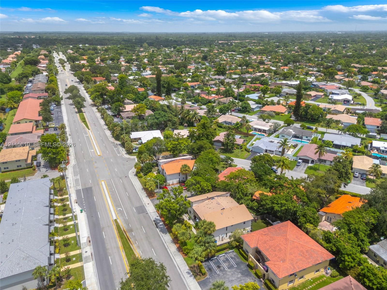 Aerial perspective of a suburban neighborhood featuring paved arterial roadways, residential clusters, mature tree canopies, tiled roof architecture, and integrated surface parking