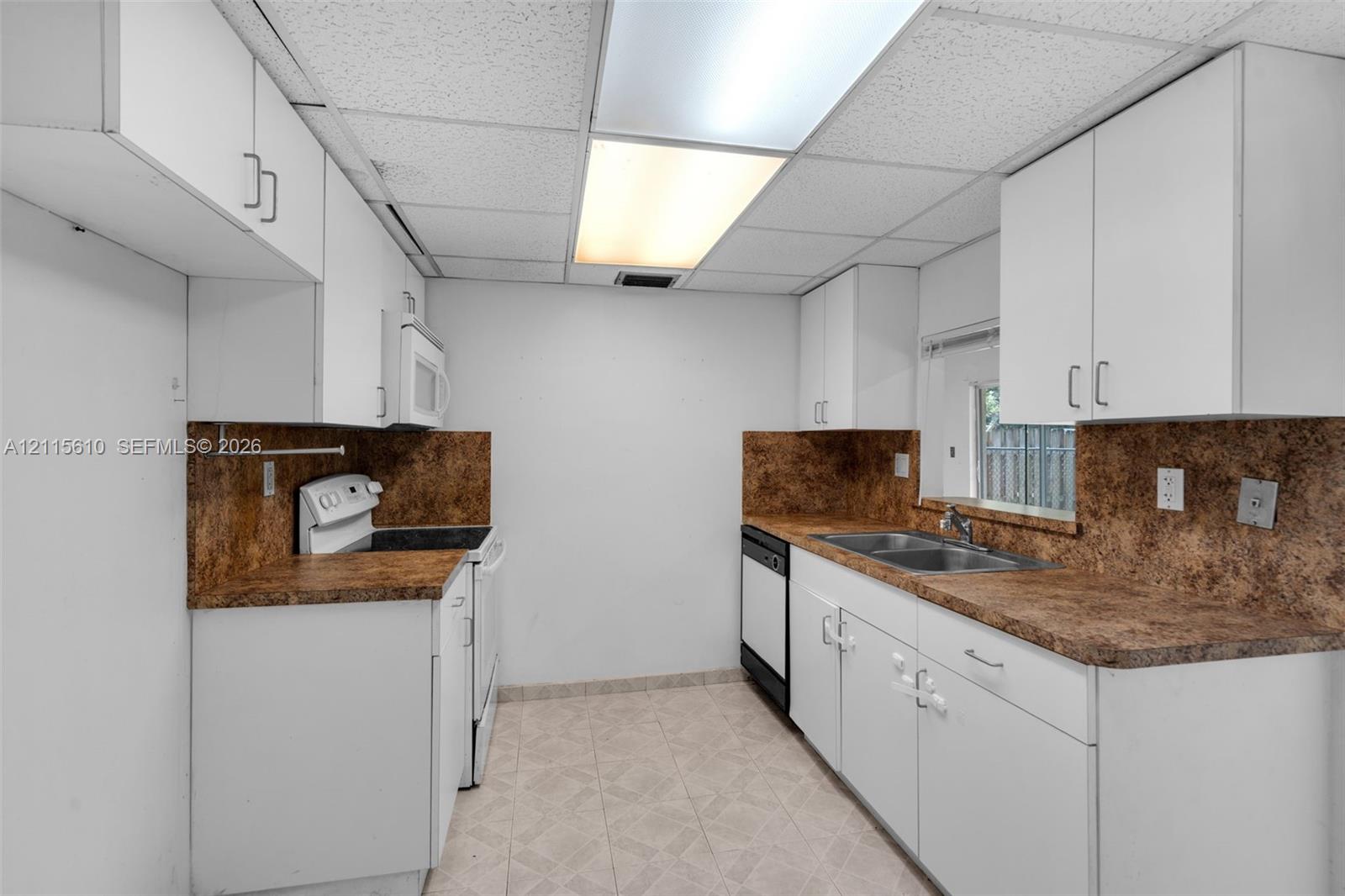 Kitchen featuring white cabinetry, patterned laminate countertops, dual-basin stainless steel sink, integrated dishwasher, and tiled flooring