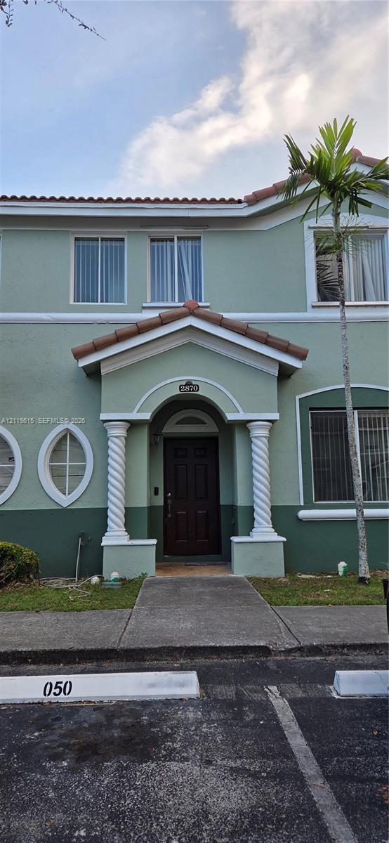 Exterior facade featuring two-tone stucco siding, decorative spiral columns, a gabled entry portico, and dual elliptical accent windows