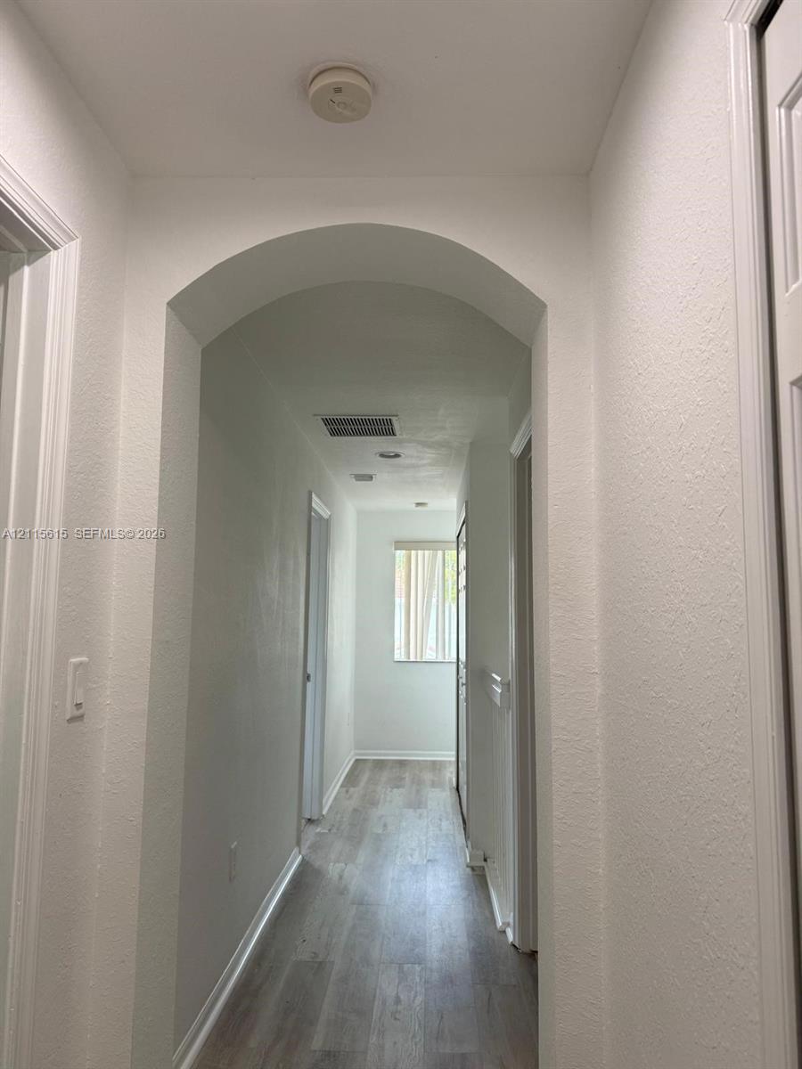 Interior hallway featuring arched architectural detailing, light-toned wood-finish flooring, and crisp white walls