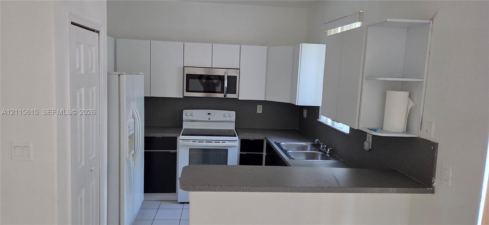 Kitchen featuring white cabinetry, stainless steel microwave, stone-finish countertops, stainless steel dual-basin sink, and a breakfast bar