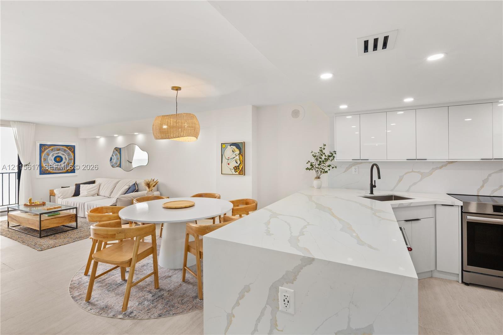 Kitchen featuring stone-finish waterfall edge island, quartz countertops with integrated backsplash, sleek white flat-panel cabinetry, and matte black plumbing fixtures