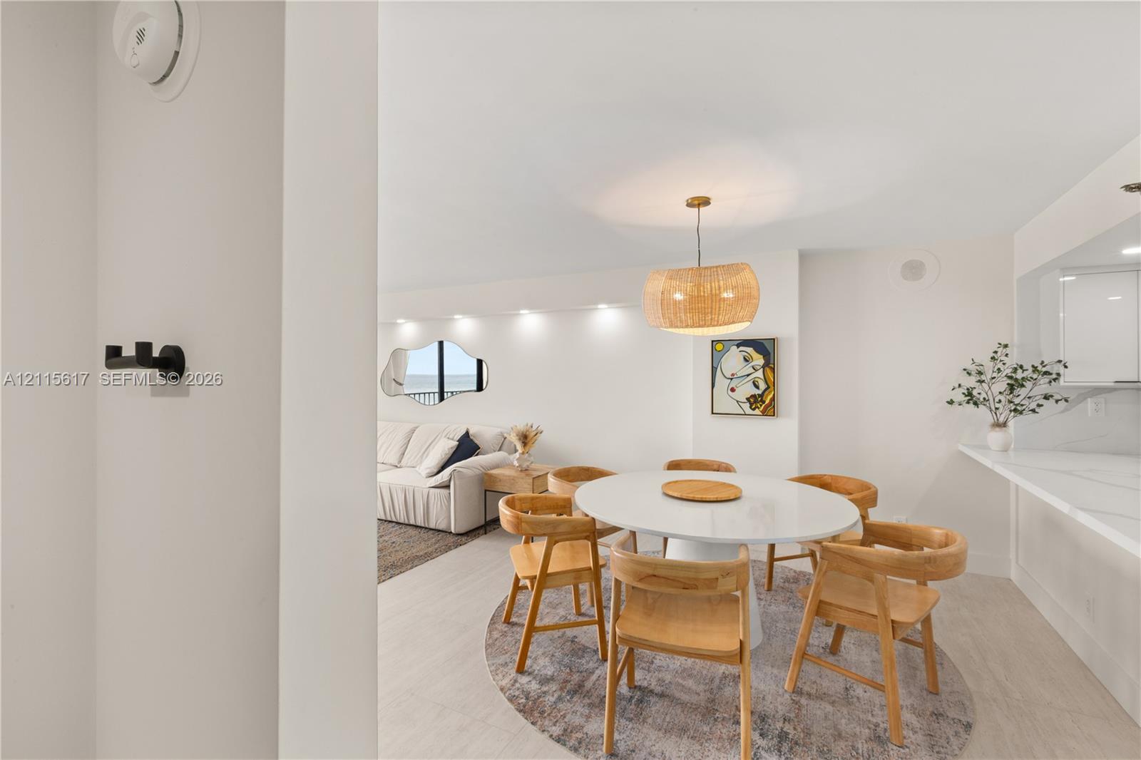 Dining area featuring light-toned flooring, recessed ceiling lighting, a woven drum pendant fixture, and a stone-surface breakfast bar