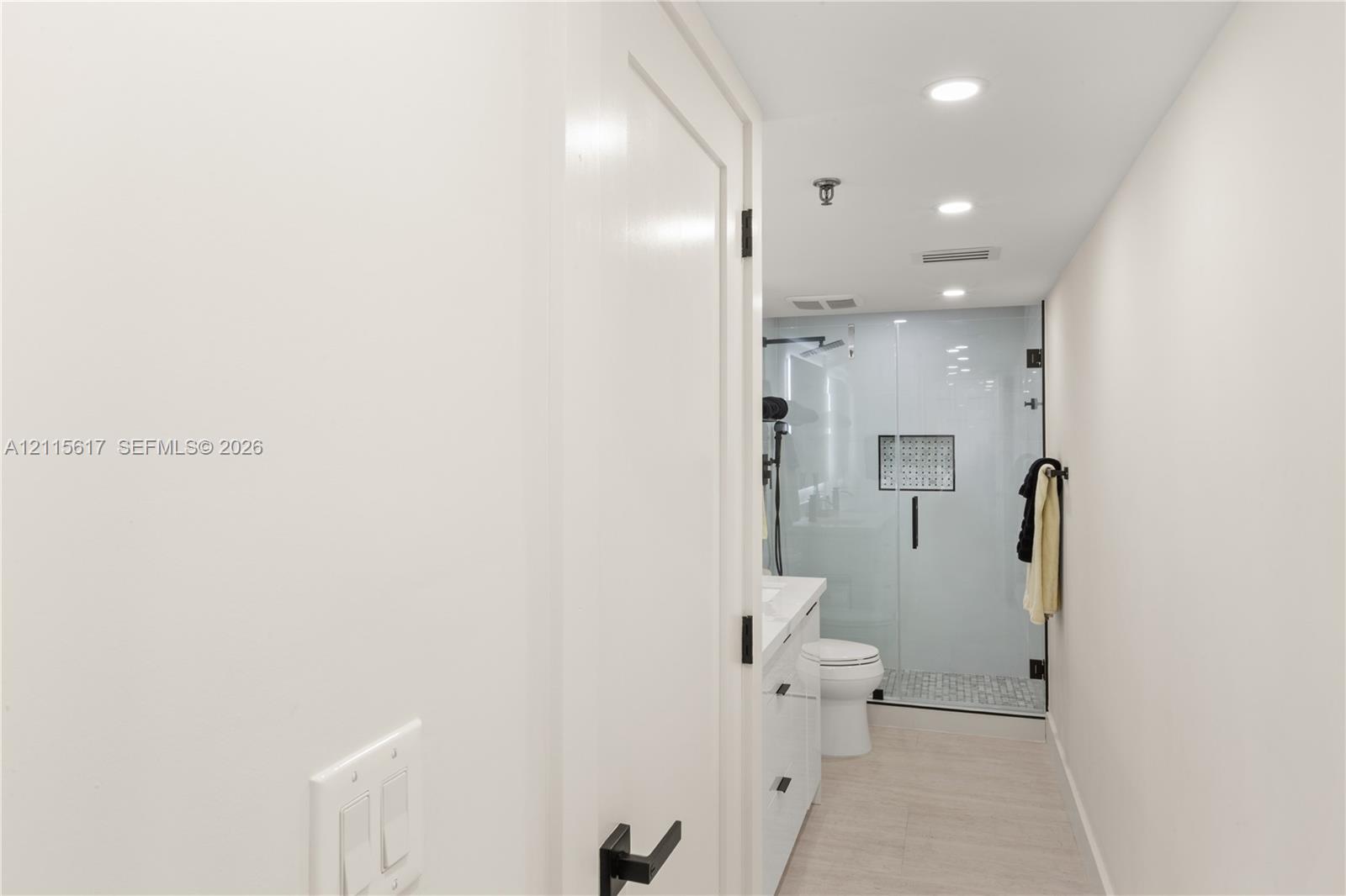 Bathroom featuring a walk-in shower with glass enclosure, built-in tiled shower niche, vanity with undermount sink, matte black hardware, and recessed lighting