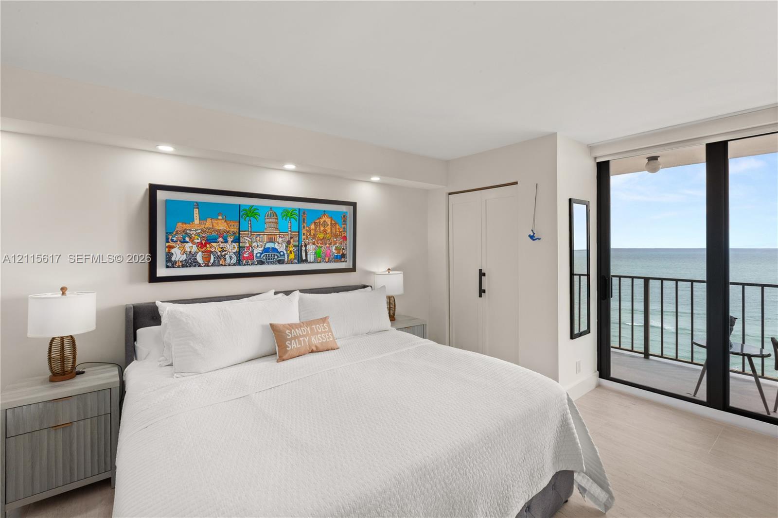 Neutral-toned interior featuring floor-to-ceiling sliding glass doors, a private balcony with metal railing, integrated recessed ceiling lighting, and large-format tile flooring
