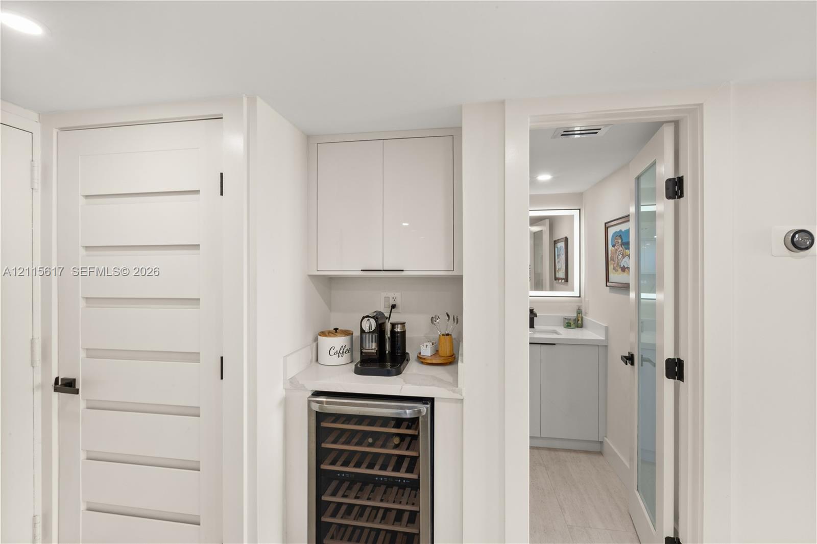 Built-in cabinetry with high-gloss finish, stone countertop, under-counter wine refrigerator, and glass-paneled interior door