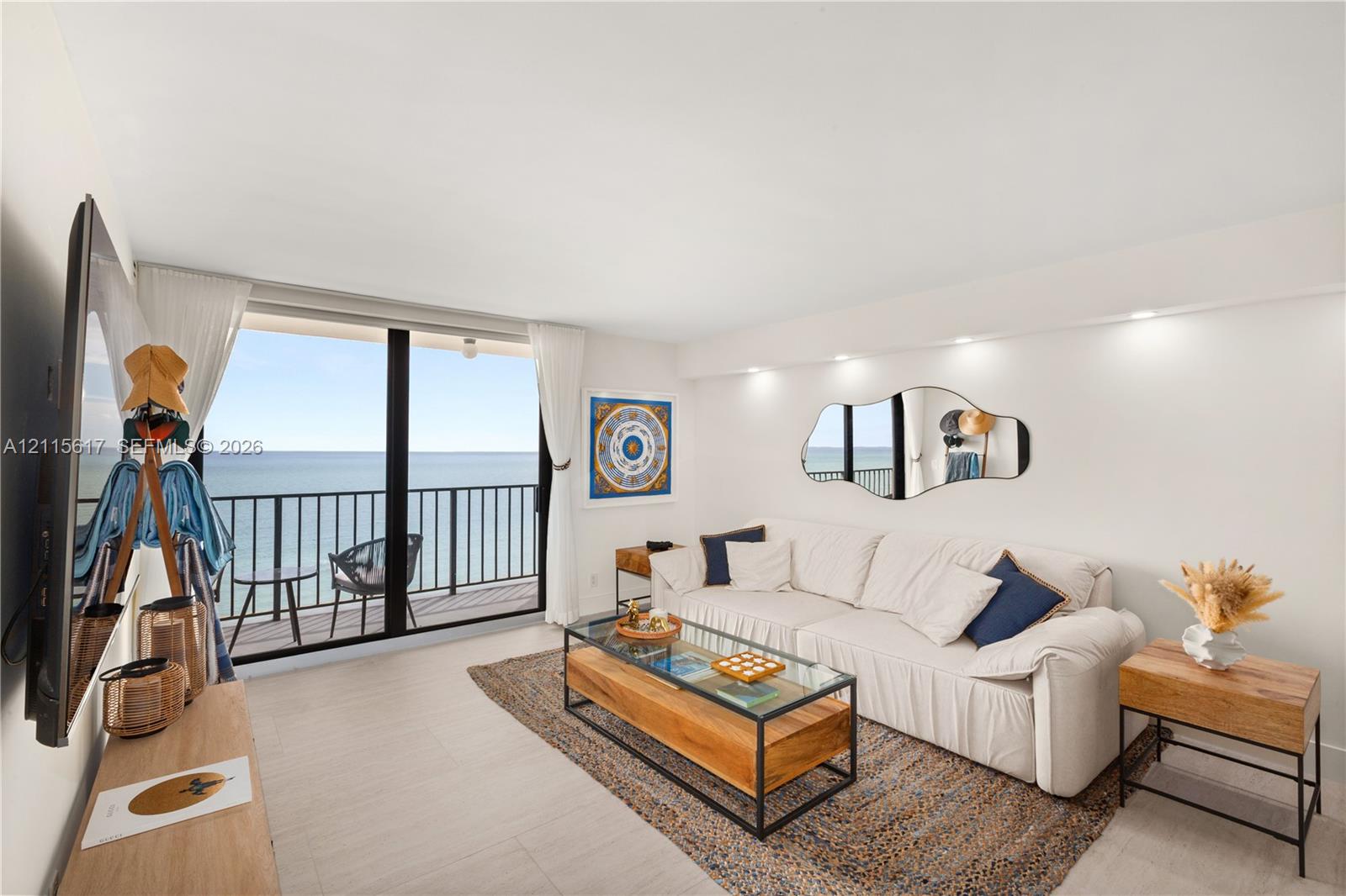 Floor-to-ceiling sliding glass doors, private balcony with metal railing, recessed ceiling lighting, wall-mounted accent mirror, and light-tone tile flooring