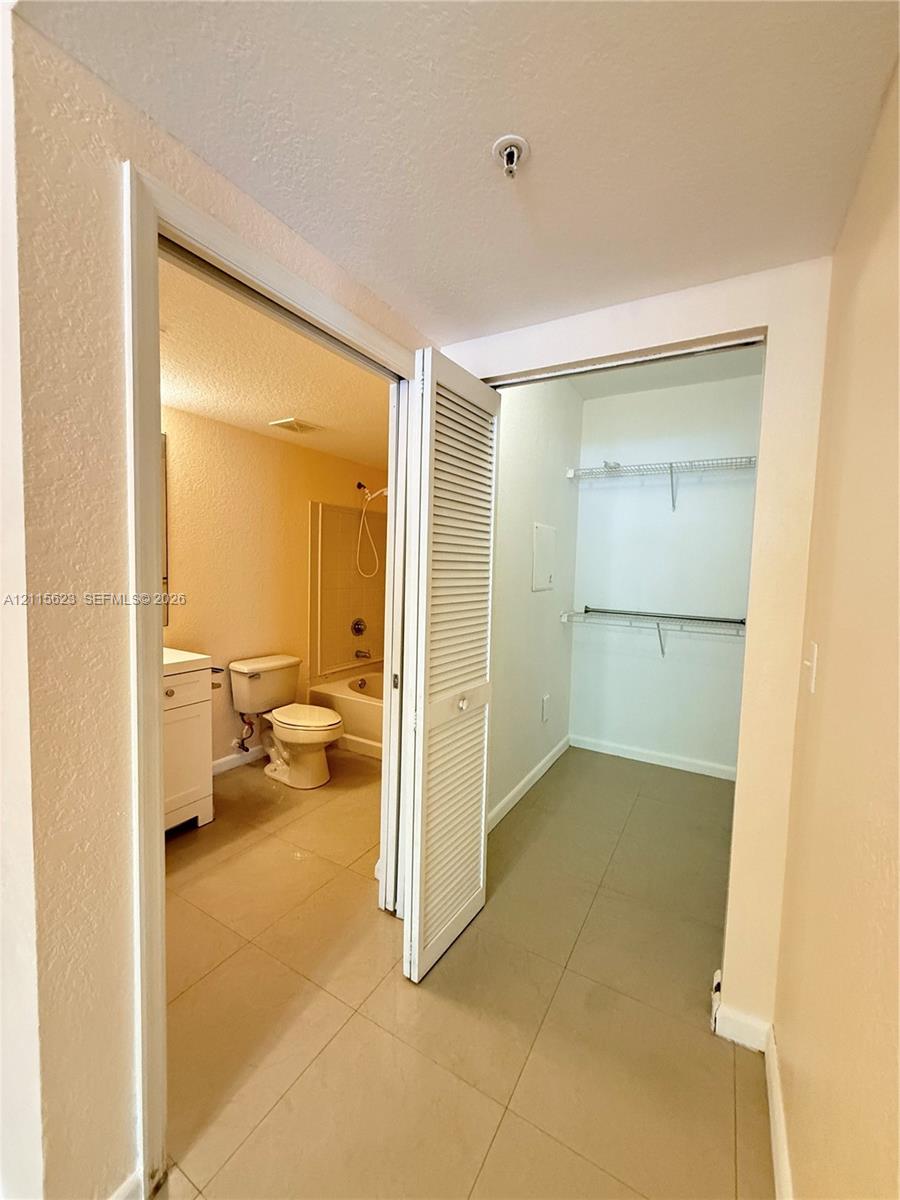 Bathroom featuring a white vanity cabinet, ceramic tile flooring, a tub-shower combination, and a walk-in closet with built-in metal shelving
